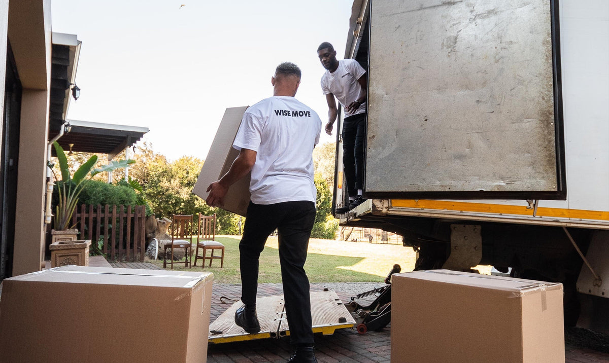 Two movers handling a carton beside an open delivery truck, with more cartons nearby