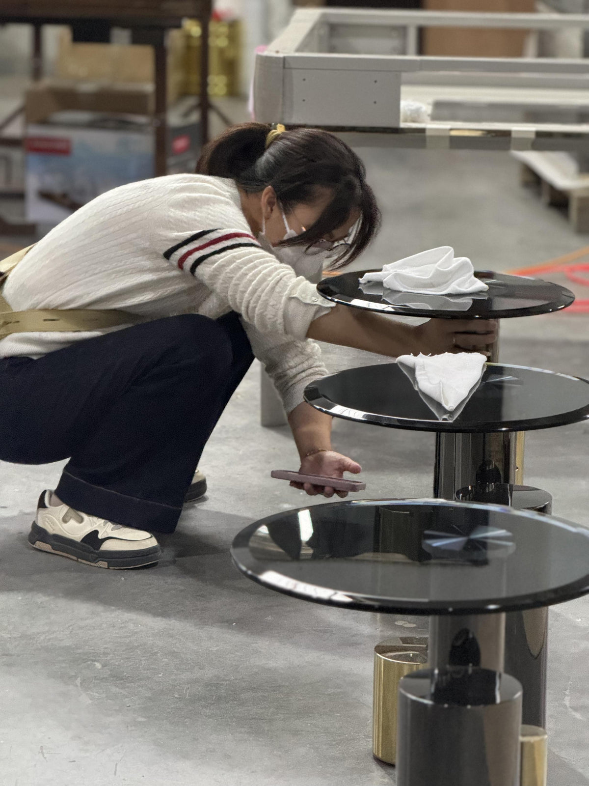 A person examining a round side table among matching tables on the workshop floor.